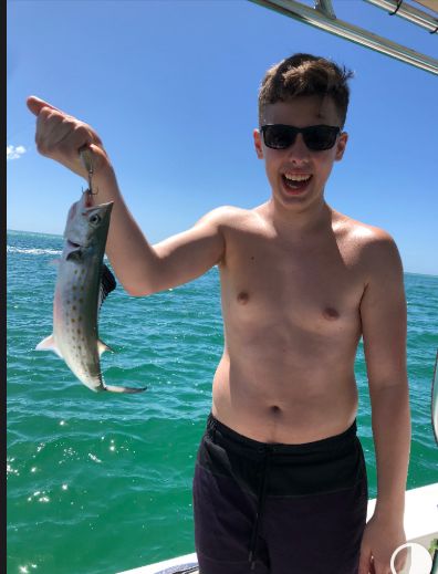 Sam as a teenager on a boat, holding up a fish